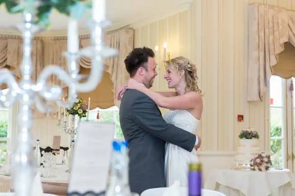 Bride and groom embracing and smiling in an elegantly decorated indoor wedding venue.