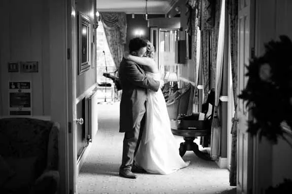 Black and white photo of a bride and groom embracing in a hallway with vintage decor.