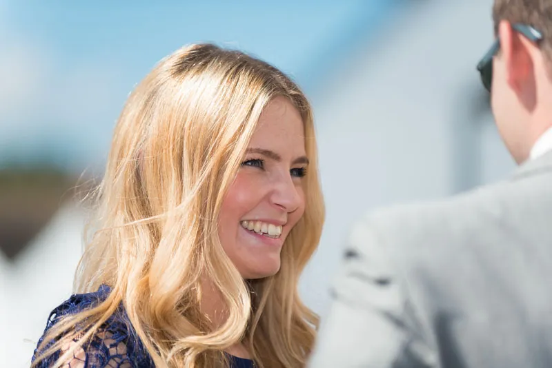 Smiling blonde woman with wavy hair wearing a blue lace dress talking to a man in a gray suit.