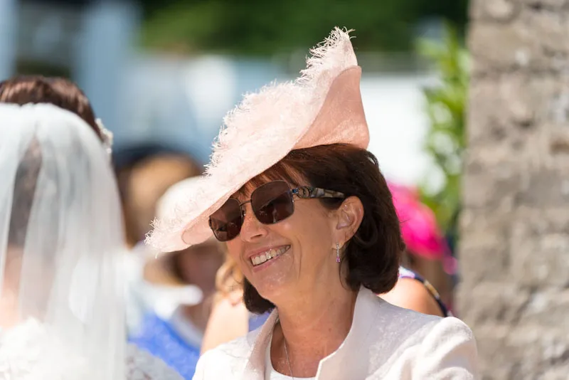 Smiling woman wearing a pink feathered hat and sunglasses at an outdoor event.