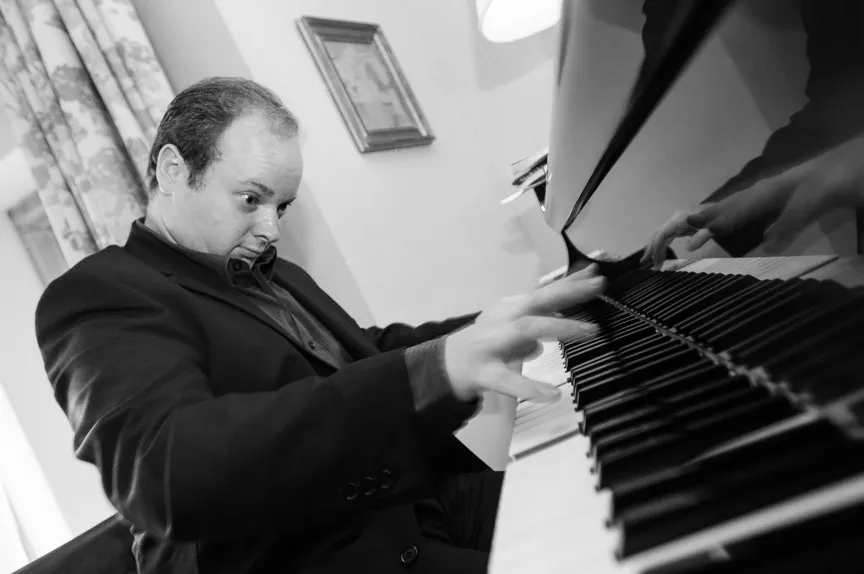 Man in a suit energetically playing a piano indoors with intense focus.