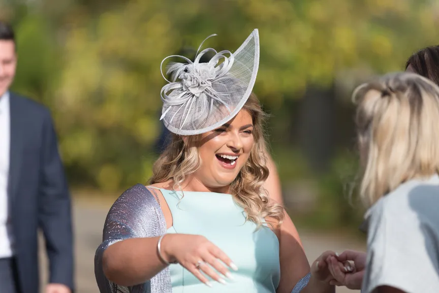 Smiling woman wearing a pale blue dress and an elaborate silver fascinator, holding hands with another person.