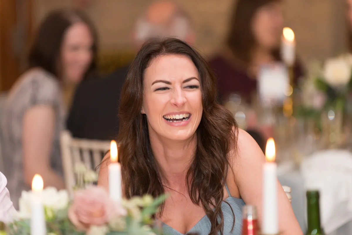 Smiling woman with long brown hair sitting at a table with lit candles and floral decorations.