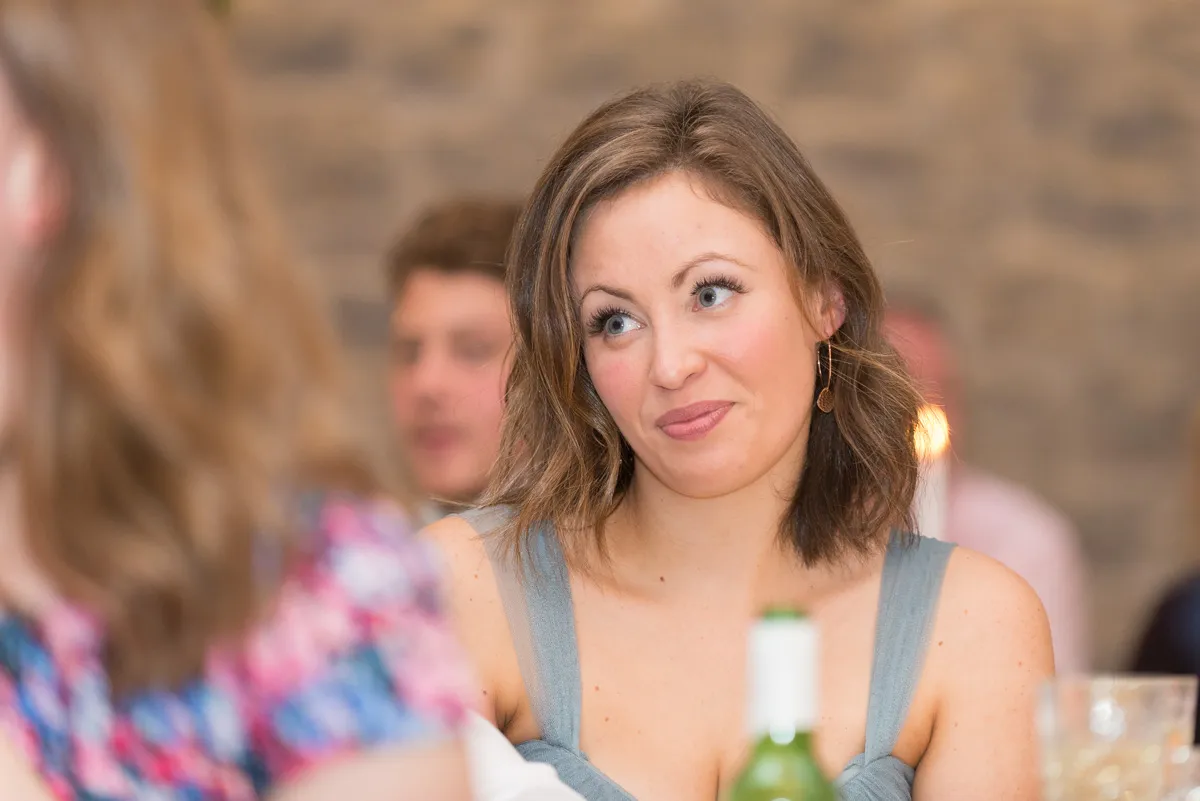 Young woman with shoulder-length hair and earrings looking thoughtfully off to the side at a social gathering.