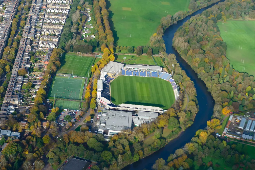 Aerial view of a football stadium surrounded by trees, a river, and nearby residential houses.