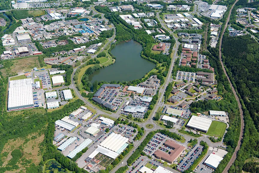 Aerial view of an industrial park with multiple warehouses, office buildings, parking lots, and a central pond surrounded by greenery.