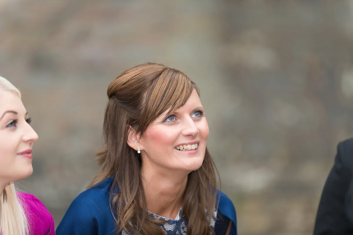 Smiling woman with brown hair and blue eyes looking upward, with another woman partially visible on the left.