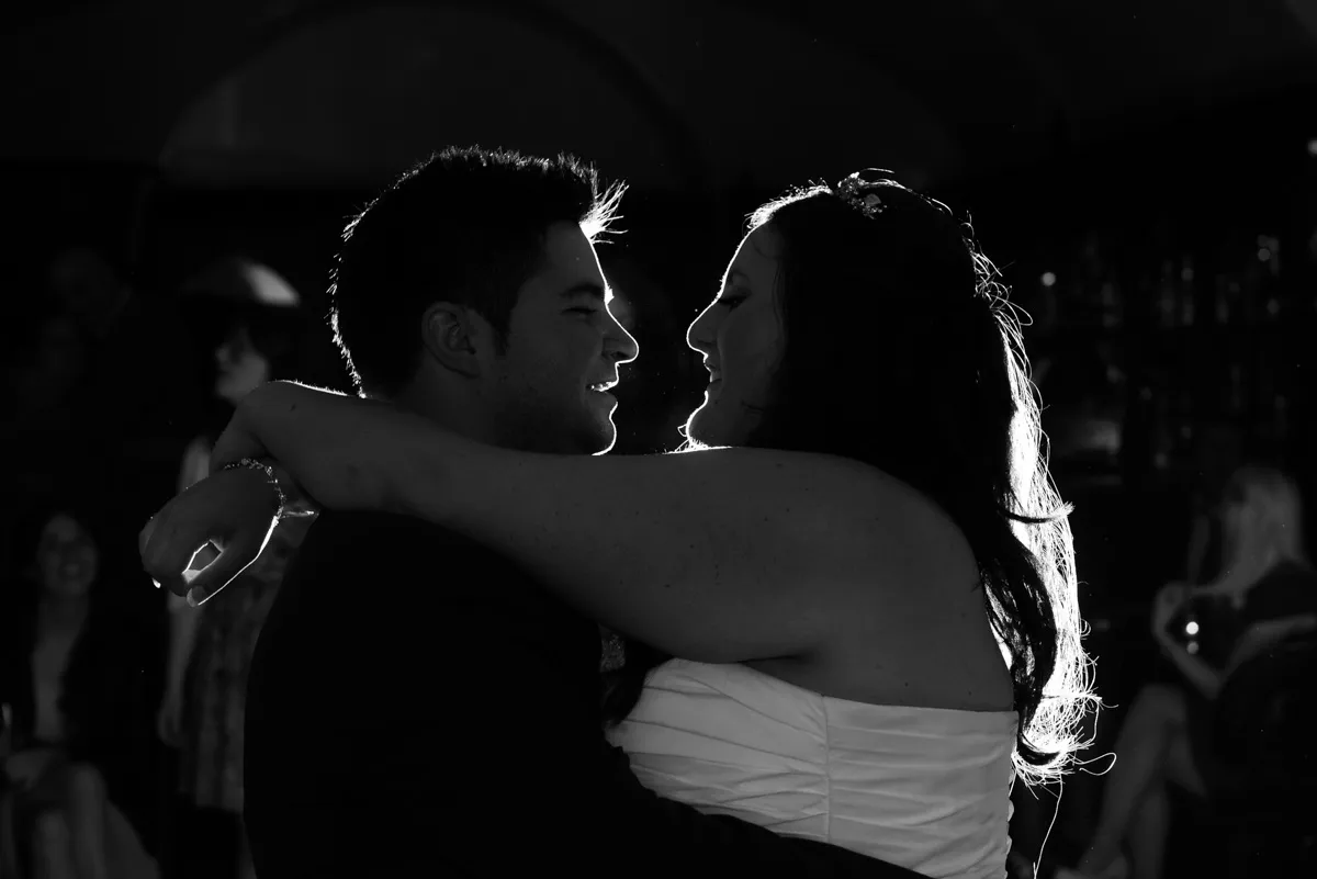Bride and groom dancing closely in a dimly lit room with people in the background.