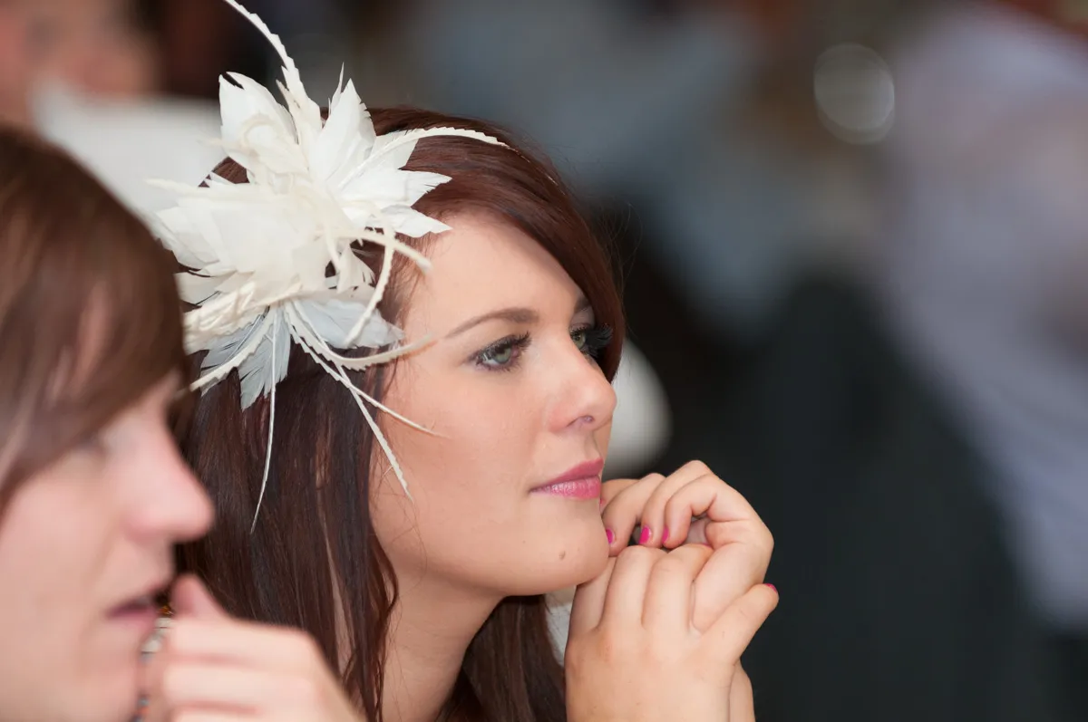 Woman with red hair wearing a white feathered hair accessory, resting her chin on her hands.