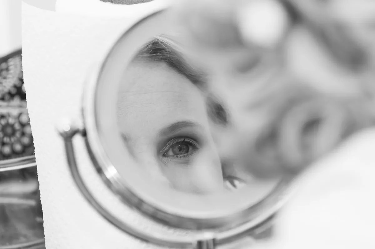 Close-up of a woman's eye reflected in a round vanity mirror in black and white.
