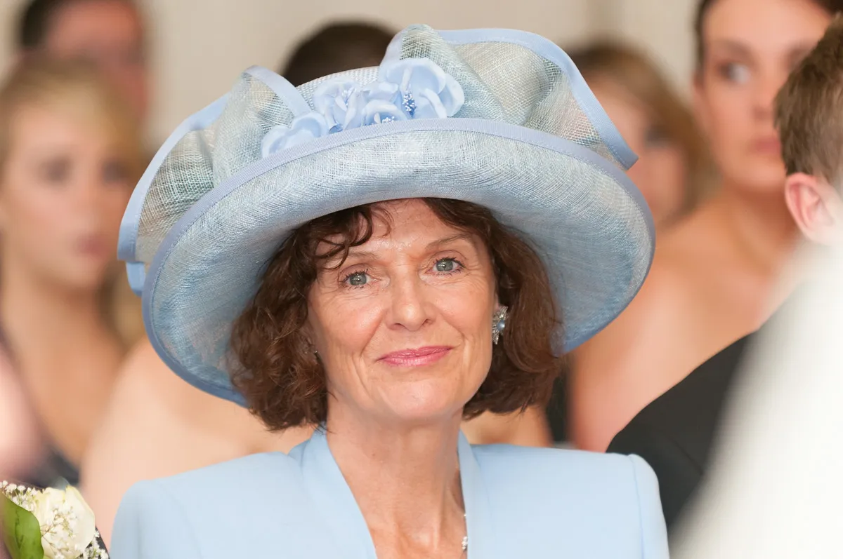 Woman wearing a large light blue hat with floral decorations and a matching light blue outfit at a formal event.