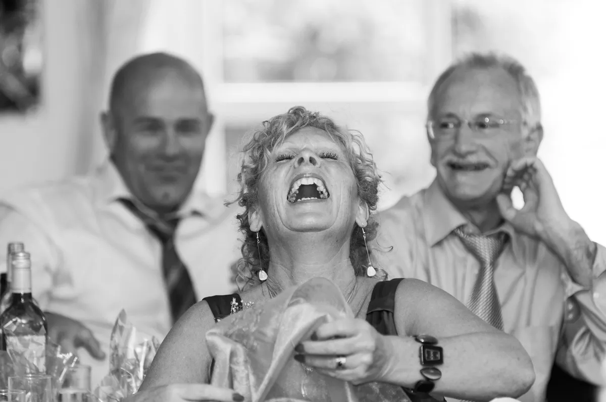 Black and white image of a woman laughing heartily with two men smiling in the background.