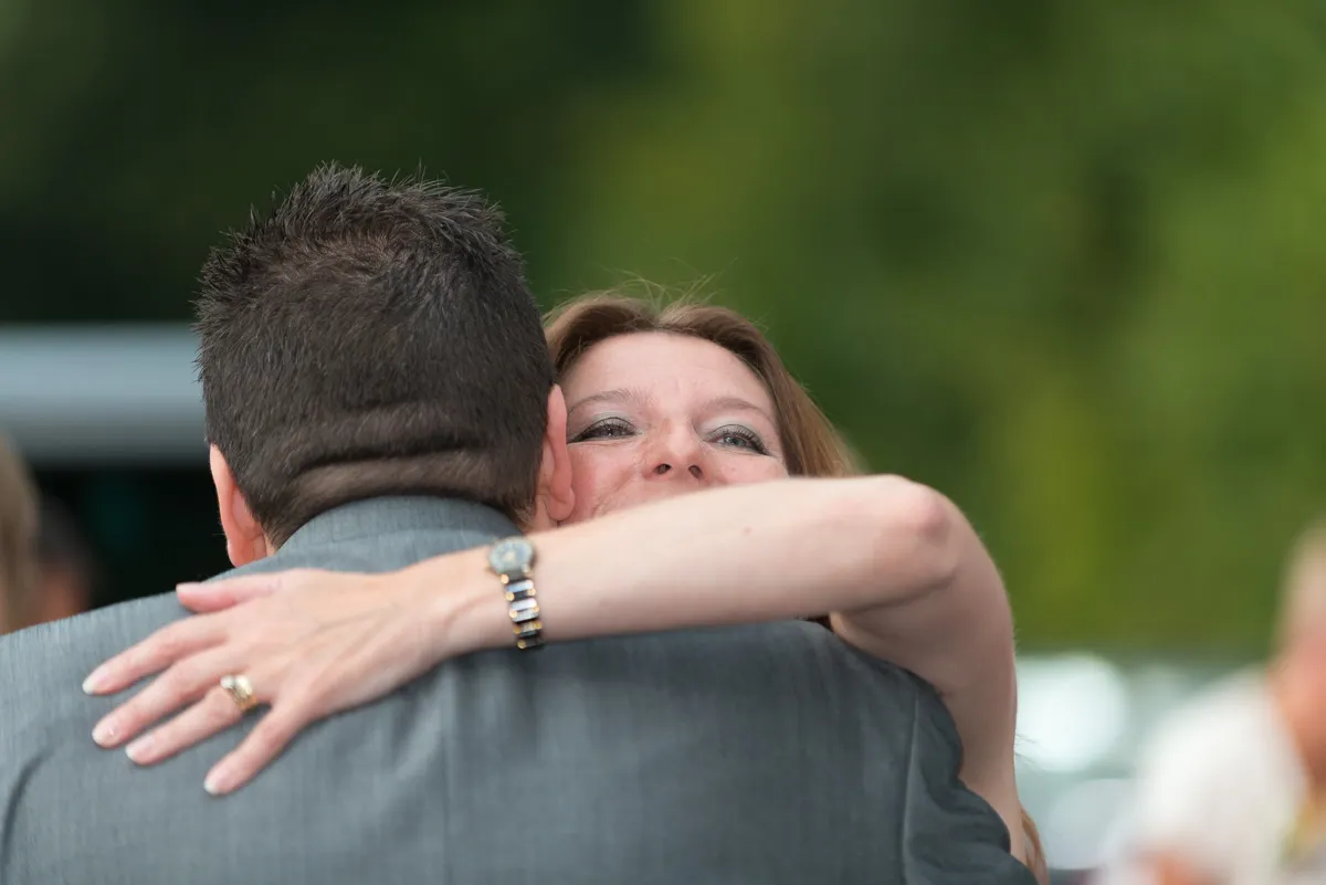 Woman hugging a man wearing a gray suit outdoors with blurred green background.