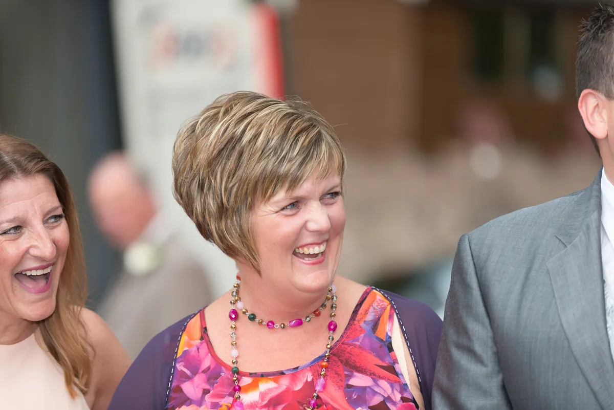 Two women smiling and laughing, one wearing a colorful floral dress and beaded necklace.
