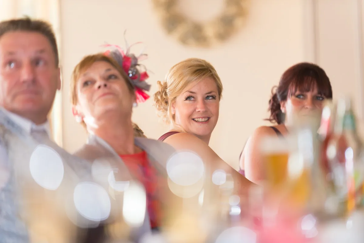 Four adults sitting at a table, with a woman in a maroon dress smiling and looking to the side.