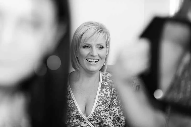 Smiling blonde woman with short hair wearing floral dress, blurred people in foreground.