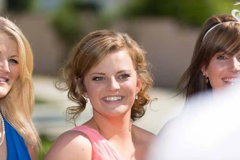 Smiling young woman with curly light brown hair wearing a pink dress at an outdoor event.