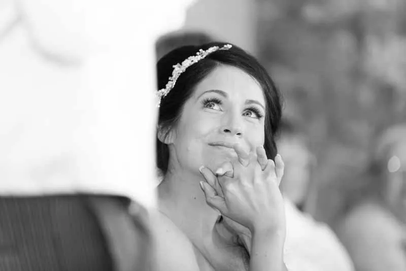 Black and white photo of a bride looking up emotionally while holding hands, wearing a hair accessory with a floral design.