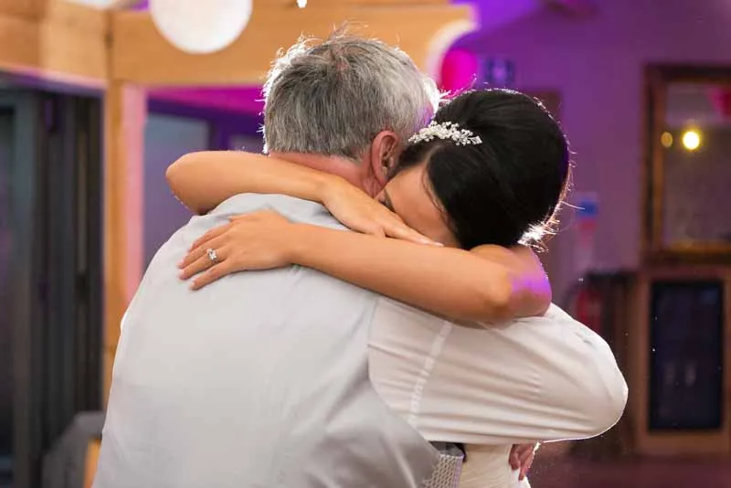 Bride embracing an older man in a heartfelt hug during a wedding reception.