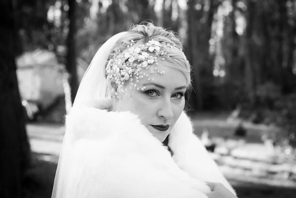 Black and white portrait of a bride wearing a veil, floral headpiece, and a fur shawl outdoors.