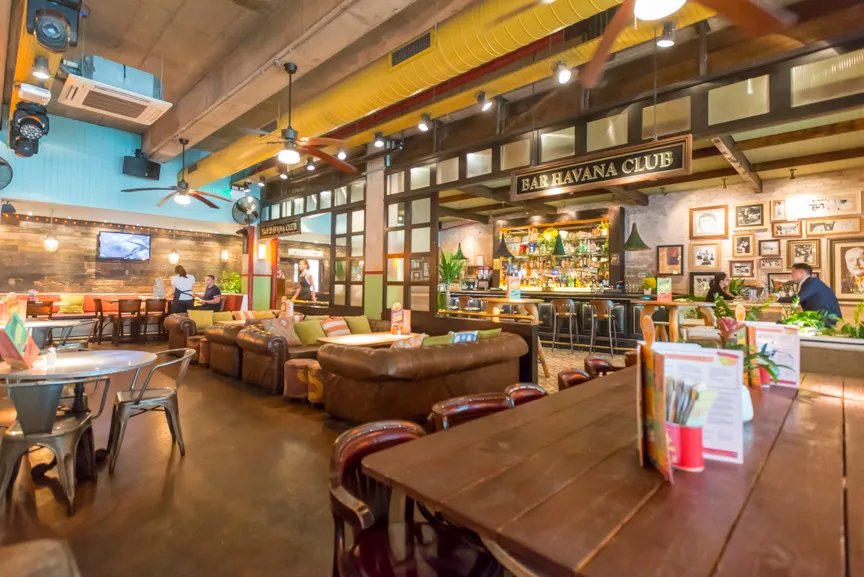 Cozy bar interior with brown leather sofas, wooden tables, and a well-stocked bar under a sign reading 'Bar Havana Club'.