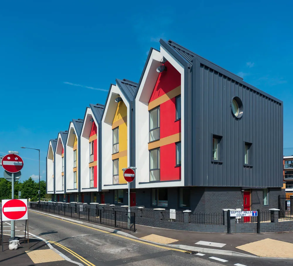 Modern row of houses with pitched roofs, featuring red, yellow, and white facades, next to a street with no entry signs.
