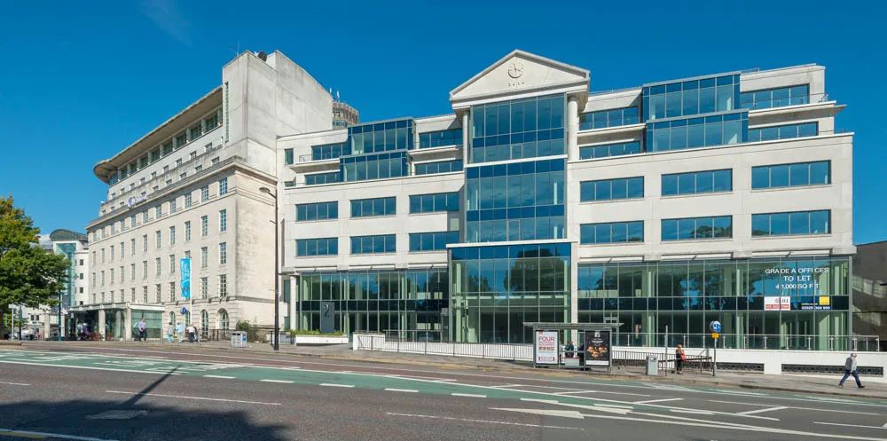 Modern office building with large glass windows and a clock on top under clear blue sky.