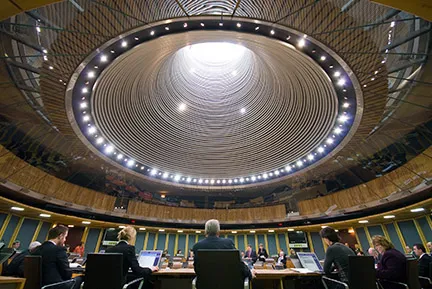 Conference room with a circular ceiling light fixture and people seated around a large table.