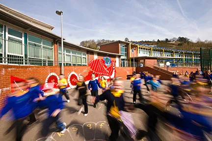 Children wearing blue uniforms running and playing outside a school building on a sunny day.