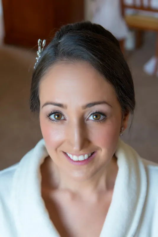 Close-up of a smiling woman with brown eyes and dark hair pinned back, wearing a white robe.