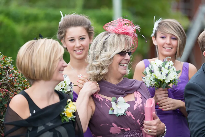 Group of women in purple dresses and floral accessories smiling and holding bouquets at an outdoor event.