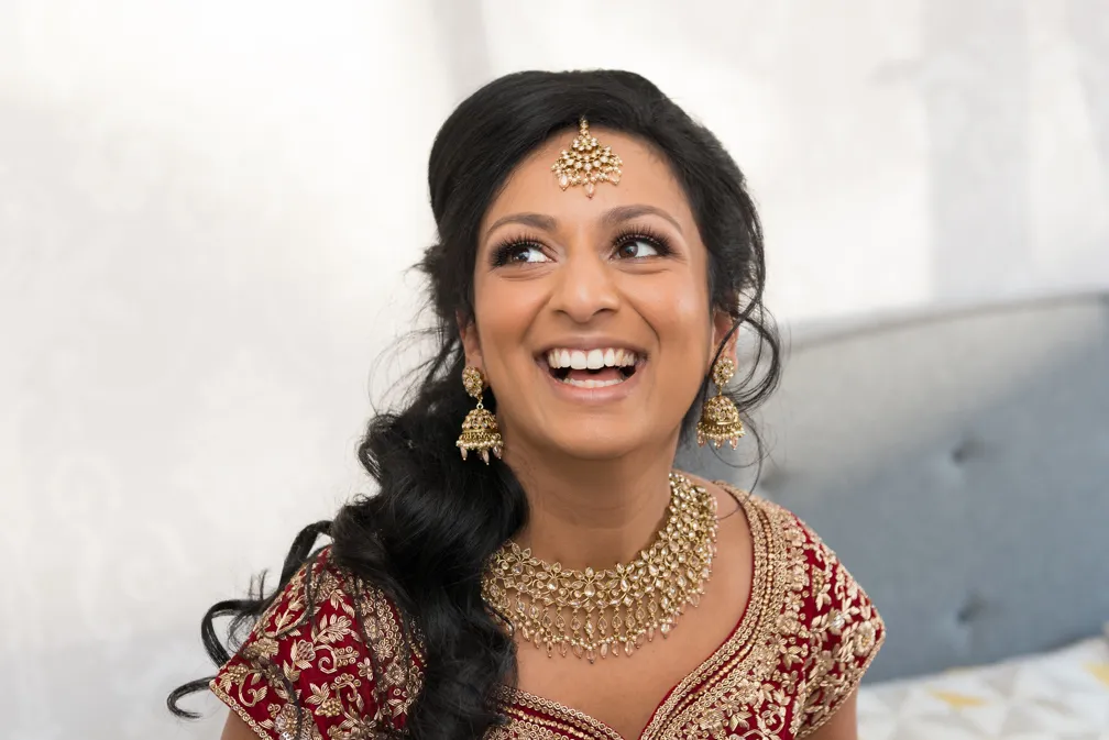 Smiling woman in red and gold traditional attire with gold jewelry and styled black hair.