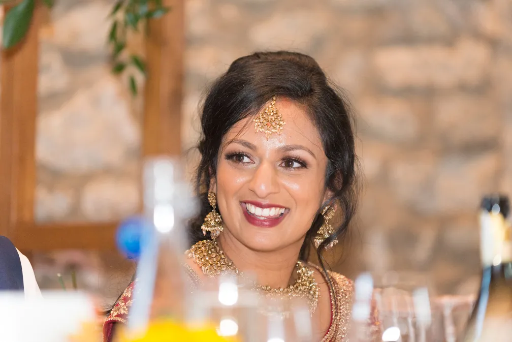 Smiling woman wearing traditional gold jewelry and a red outfit at a festive event.