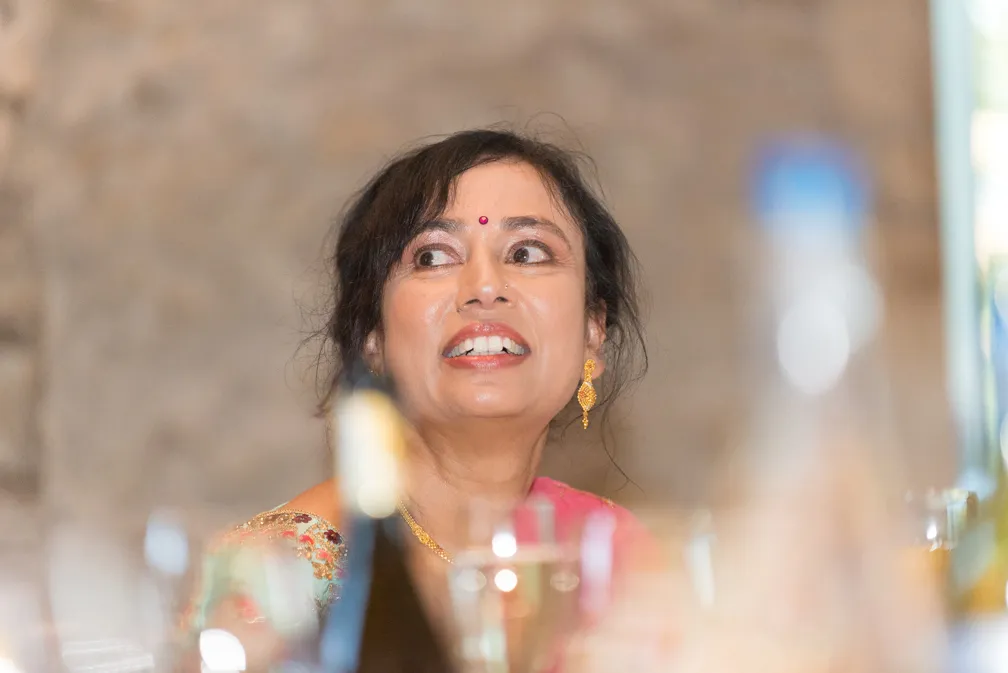 Woman wearing gold earrings and a pink saree with a red bindi, looking to her right with a smile.