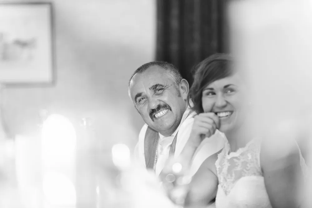 Black and white photo of a smiling man with a mustache and a woman in a lace dress laughing together.