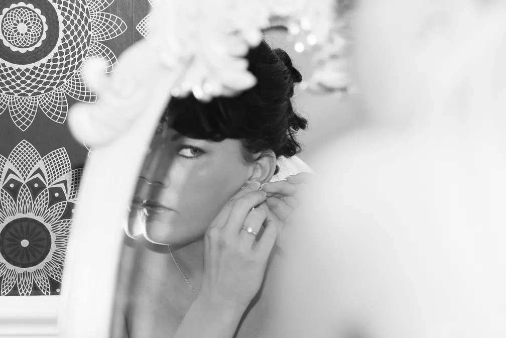 Woman looking into an ornate mirror while adjusting an earring, with a patterned background.