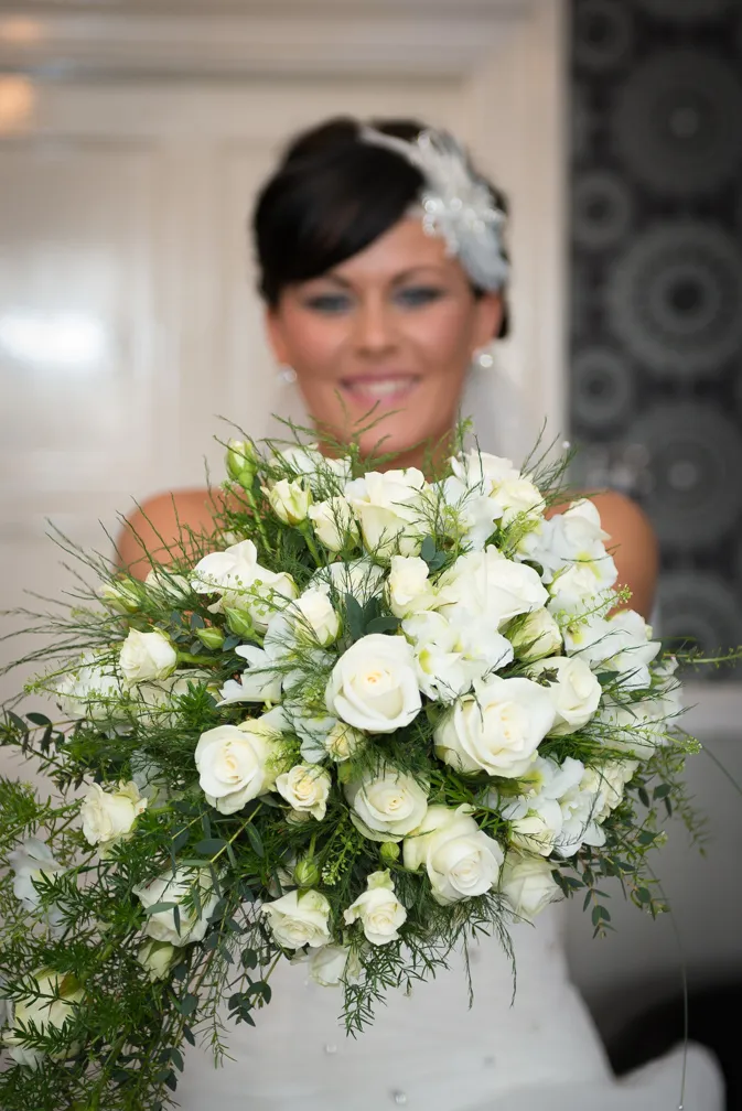 Bride holding a large bouquet of white roses and green foliage.