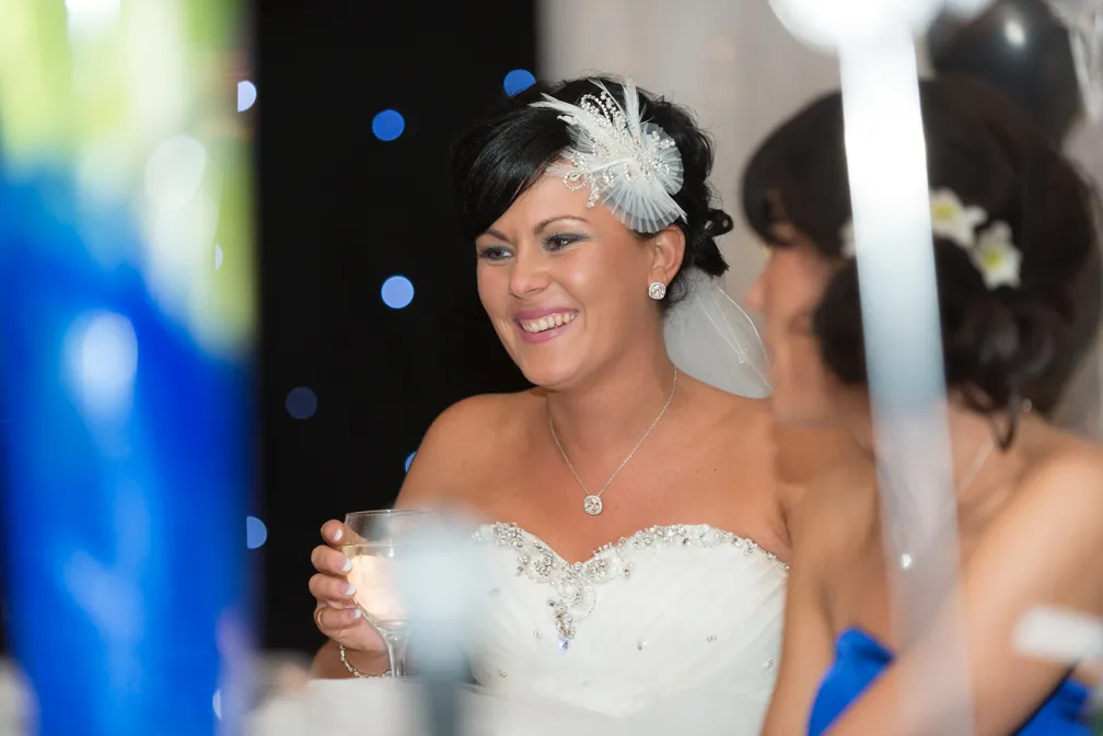 Smiling bride in a white strapless wedding dress holding a glass, with decorative hairpiece and veil.