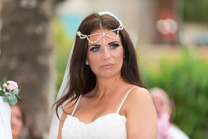 Brunette bride with blue eyes wearing a white lace wedding dress and a pearl headpiece with veil.