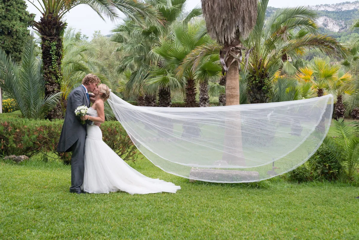 Bride and groom kissing in a lush garden with the bride's long veil flowing behind her.