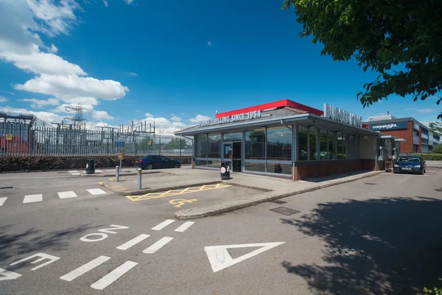 Burger King restaurant building with a red roof and a parking lot under a clear blue sky.