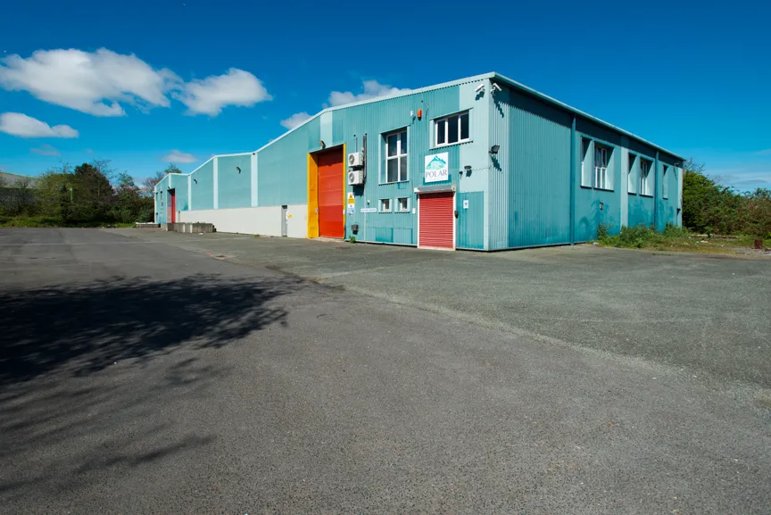 Blue industrial warehouse with red and orange doors under a partly cloudy sky.
