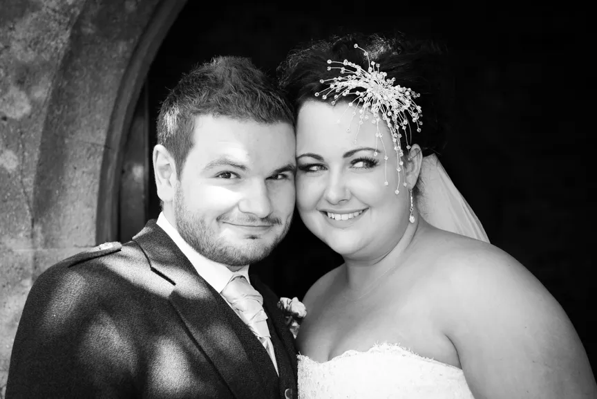 Smiling bride and groom posing closely together on their wedding day, bride wearing decorative hairpiece.