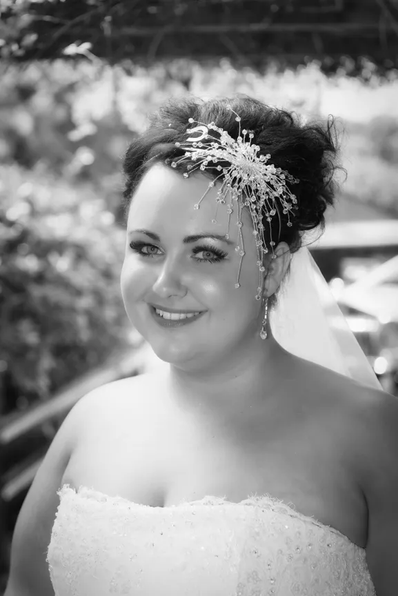 Smiling bride wearing a strapless wedding dress and decorative hairpiece with veil in an outdoor setting.