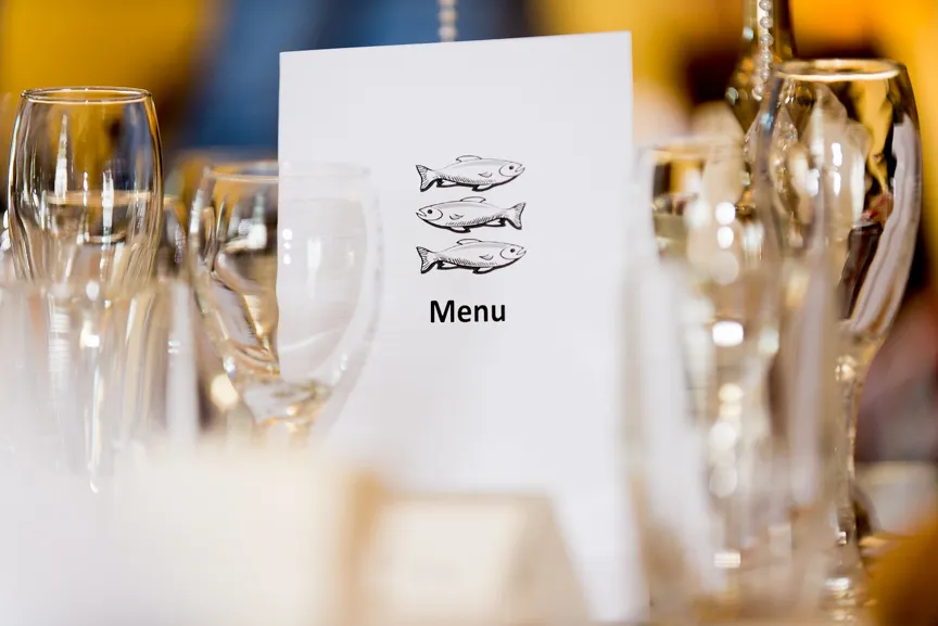 White menu card with three fish illustrations and the word 'Menu' on a table surrounded by empty glassware.
