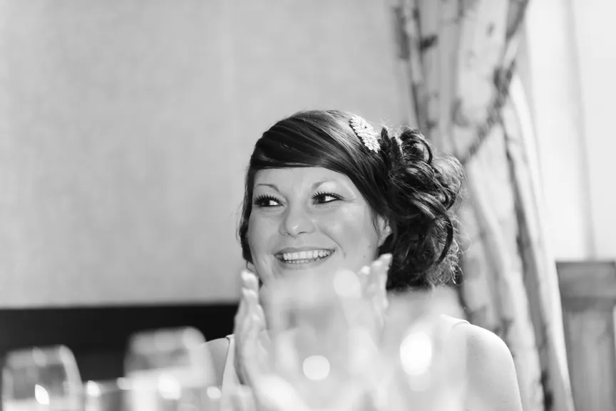 Smiling woman with styled hair and a hair clip, clapping her hands indoors near a window with curtains.