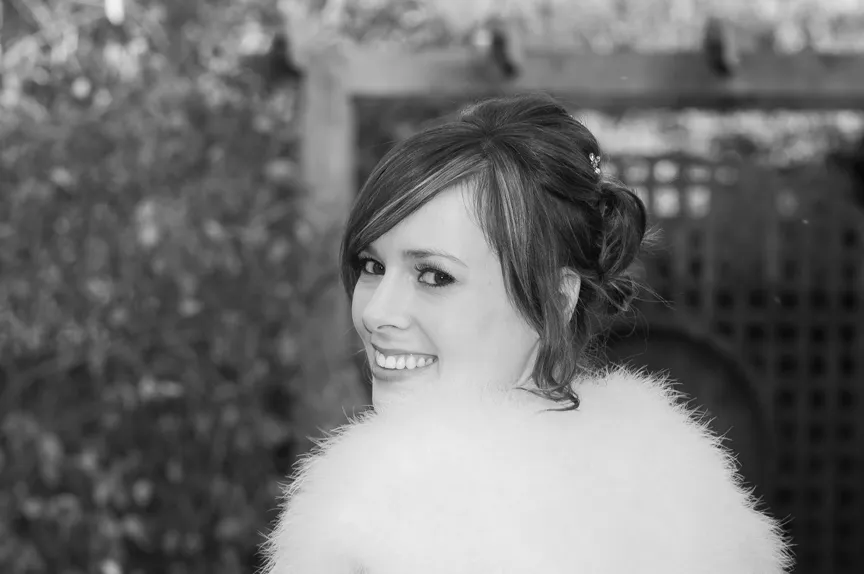 Smiling woman with stylish updo hairstyle wearing a fluffy white garment, looking over her shoulder outdoors.