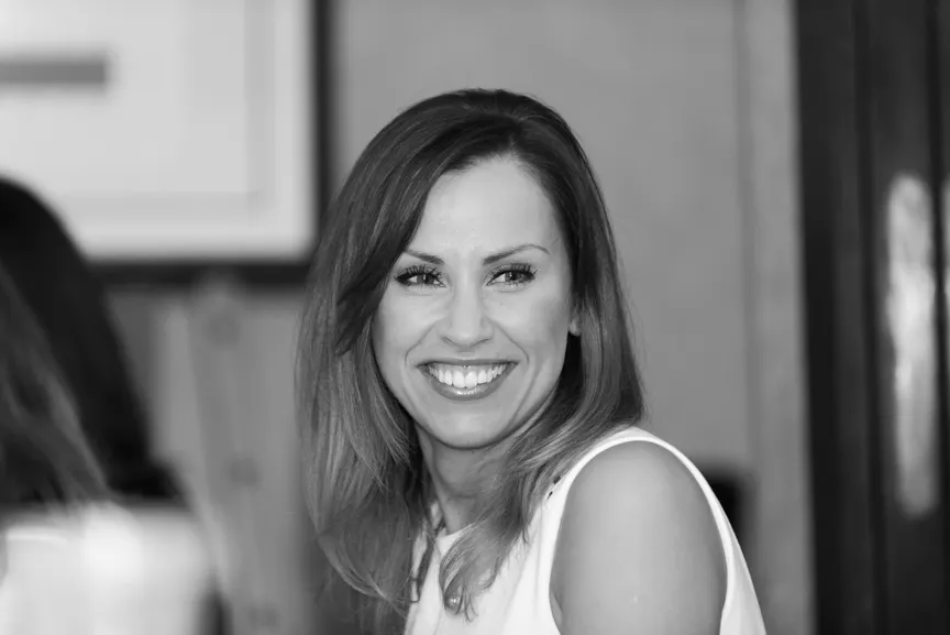 Smiling woman with shoulder-length hair wearing a sleeveless top in a black and white photo.