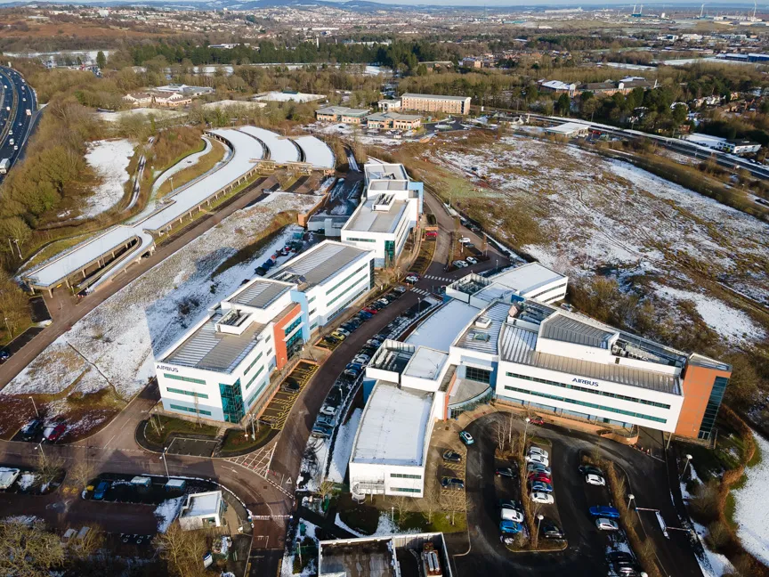 Aerial view of Airbus office buildings surrounded by parking lots with light snow on the ground and trees, with a highway visible to the left.