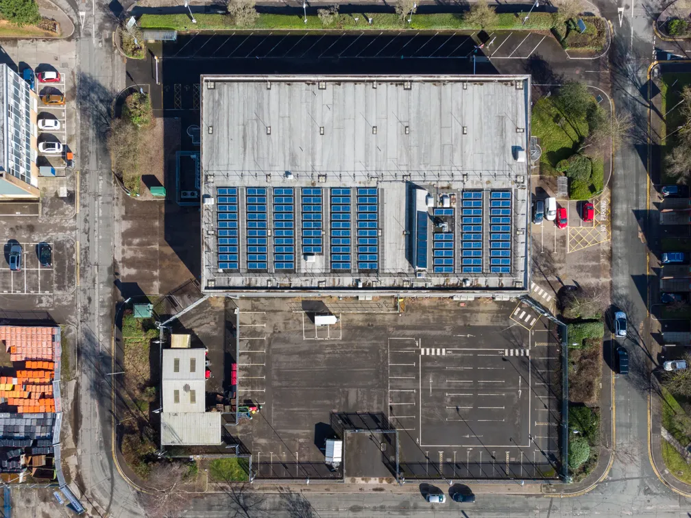 Aerial view of a large building with solar panels on the roof and an adjacent empty parking lot.